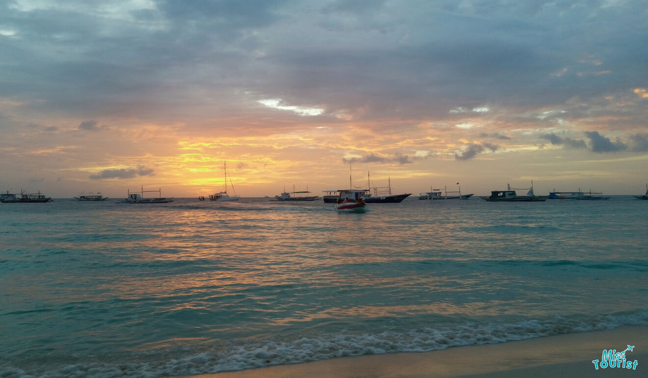 A breathtaking sunset at a beach, displaying orange and pink hues in the sky with traditional Filipino boats floating near the shore.